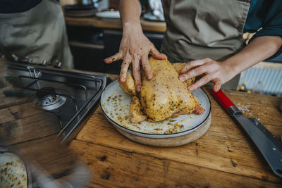 Chef marinating chicken meat while standing by colleague in kitchen