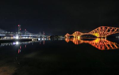 Illuminated bridge over river in city against sky at night