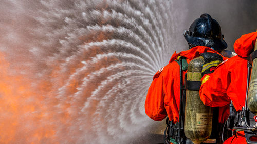 Rear view of firefighters spraying water on fire