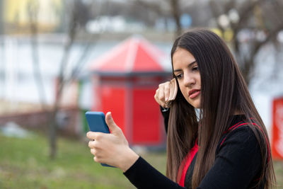 Cute lovely teen girl brushing her hair and smiling  while looking at the smart phone as a mirror 