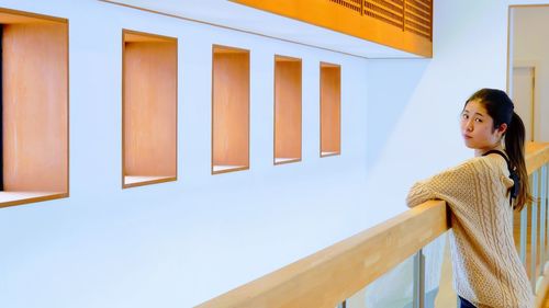 Portrait of woman leaning on railing against wall