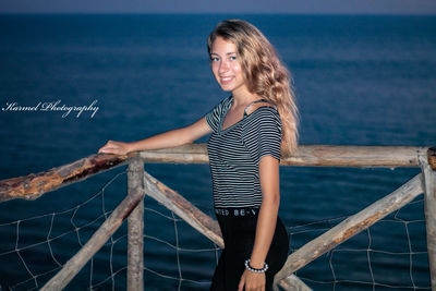 Portrait of smiling woman standing by railing against sea