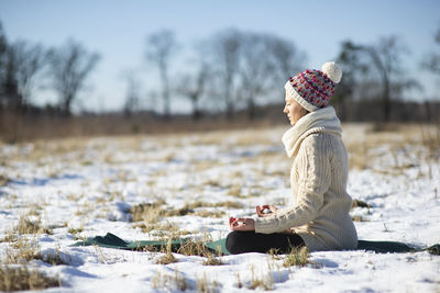 Young athletic woman sitting and meditatingin the yoga pose on snowy field during winter or spring
