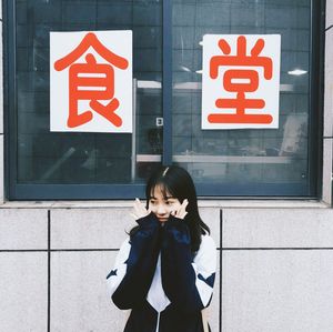 Young woman with hands on chin standing against wall