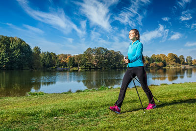 Full length of young woman exercising on field against sky