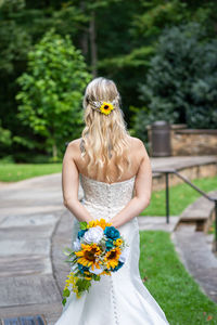 Rear view of bride holding bouquet while standing outdoors