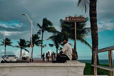 People sitting by palm trees against sky