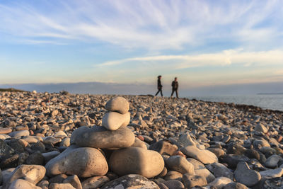 Rocks at beach with people in background against sky