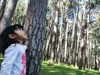 Side view of girl standing by tree in forest