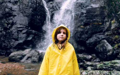 Portrait of girl standing on rock against waterfall