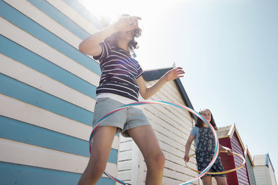 Friends spinning hula hoop against beach huts on sunny day during vacation