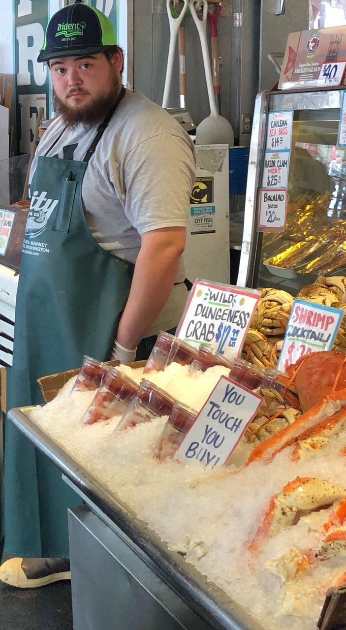 food, food and drink, business, occupation, retail, real people, store, text, one person, freshness, indoors, men, communication, waist up, cap, standing, unhealthy eating, market, ready-to-eat, pizza