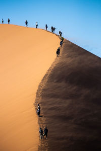 People walking on sand dune against clear blue sky