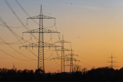 Low angle view of silhouette electricity pylon against sky during sunset