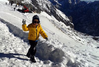 Portrait of boy playing on snowcapped mountain during sunny day