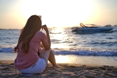 Rear view of woman sitting at beach during sunset