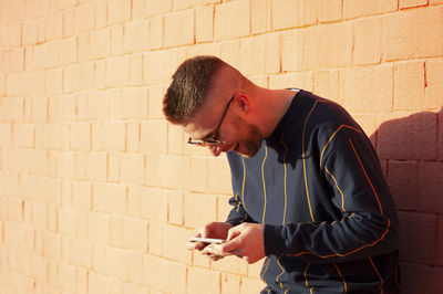 Man using phone while standing against orange brick wall