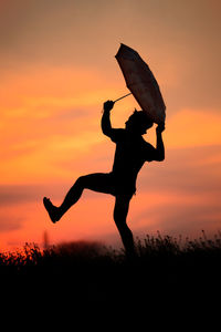 Silhouette man with umbrella against sky during sunset
