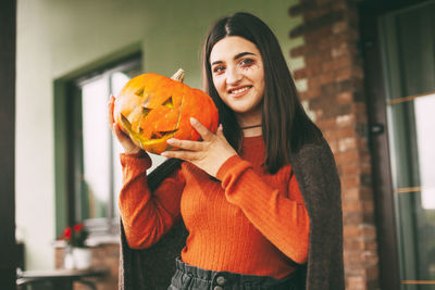 Portrait of smiling young woman holding orange while standing outdoors