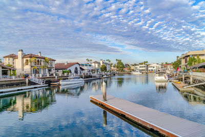 Boats moored in river by buildings against sky