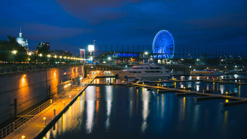 Illuminated city by river against sky at night