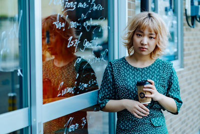 Young woman using mobile phone while standing by window