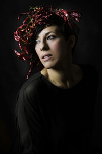 Close-up of young woman wearing red chili peppers against black background