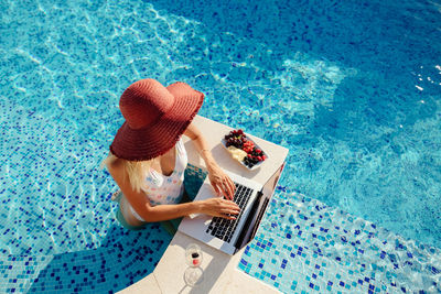 Woman using laptop while relaxing in pool