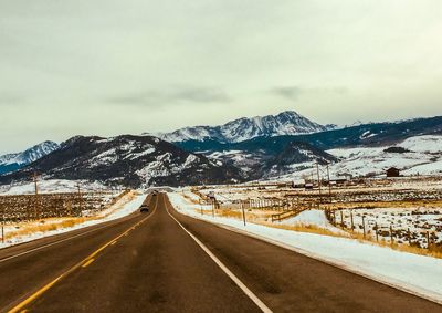 Road leading towards snowcapped mountains against sky