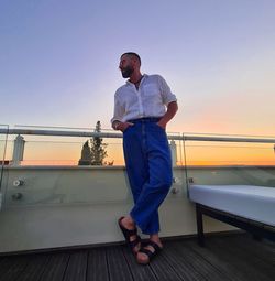 Full length of man standing by railing against sky during sunset