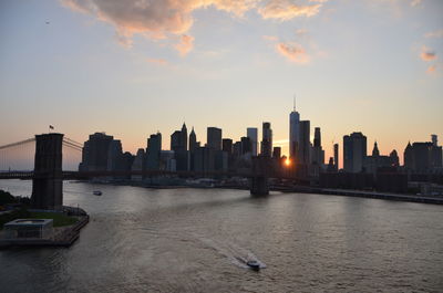 Scenic view of river by buildings against sky during sunset