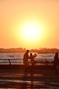 Silhouette people on beach against orange sky