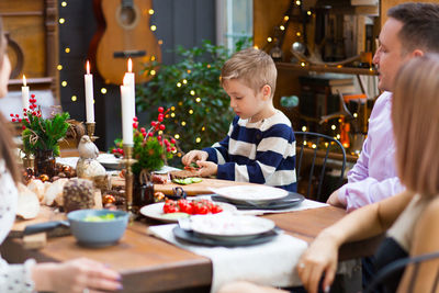 Cute boy sitting at dining table with family