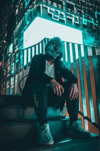 Low angle view of man sitting on stairs against illuminated light