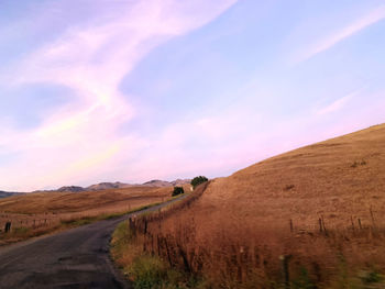 Road amidst field against sky during sunset