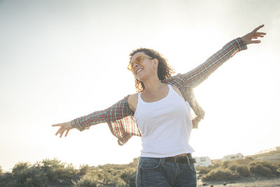 Smiling woman with arms outstretched standing against clear sky