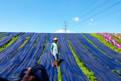 Man drying blue fabrics on grassy field against blue sky during sunny day
