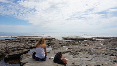 Rear view of woman sitting on beach against sky