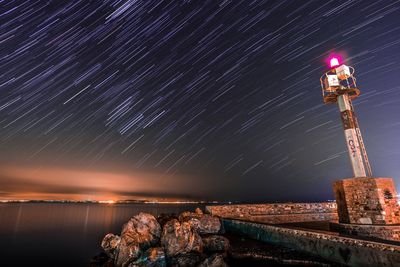 Illuminated lighthouse by sea against sky at night