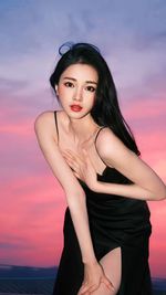 Portrait of young woman looking away against sky during sunset