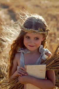 Girl child in a dress and a wreath on her head stands on a mown field of wheat at sunset in summer