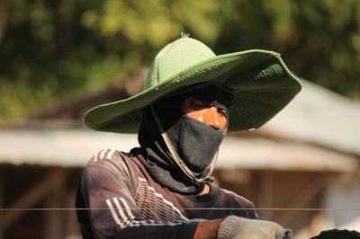 Woman wearing hat and mask while standing by fence