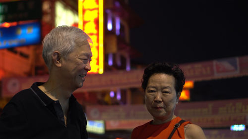 Portrait of man and woman looking at illuminated night