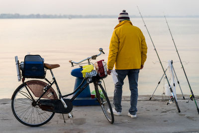 Rear view of men with bicycle on shore against sky