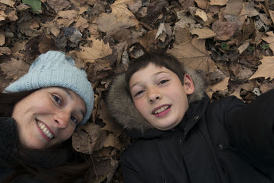 High angle portrait of smiling mother and son lying on autumn leaves
