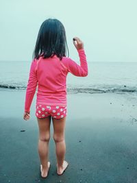 Rear view of girl standing on beach against clear sky