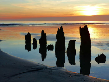 Silhouette rocks on beach against sky during sunset