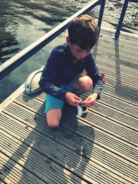 High angle view of boy crouching on pier