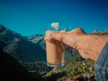 Midsection of person holding drink against blue sky