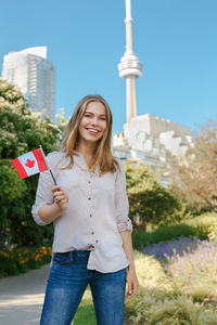 Portrait of smiling woman holding canadian flag while standing against plants